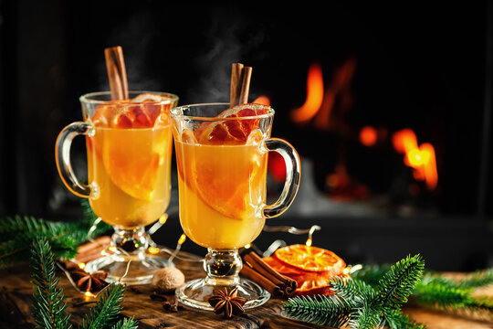 Mulled cider glasses on the background of fireplace fire. Hot mulled spiced apple cider cocktail for winter or autumn time.