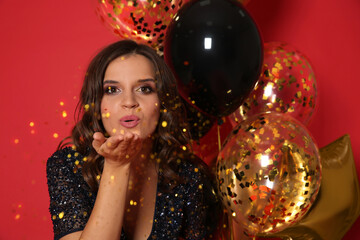 Obraz na płótnie Canvas Happy woman with air balloons blowing glitter on red background. Christmas party