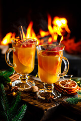 Mulled cider glasses on the background of fireplace fire. Hot mulled spiced apple cider cocktail...
