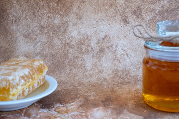 glass jar full of honey, plate with honeycomb on light brown background