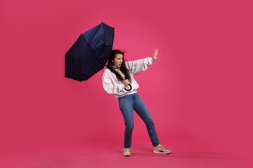 Emotional woman with umbrella caught in gust of wind on pink background