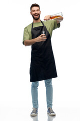 alcohol drinks, people and job concept - happy smiling barman in black apron with shaker and glass...