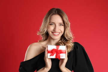 Fototapeta premium Beautiful young woman with Christmas present on red background