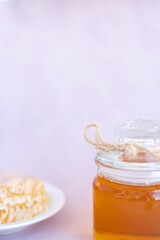 glass jar full of honey, plate with honeycomb on light brown background