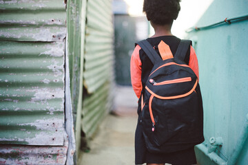 Child with back pack by shacks