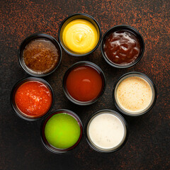 Set of sauces - ketchup, mayonnaise, mustard soy sauce, bbq sauce, pesto, mustard grains and pomegranate sauce on dark rusty stone or metal background.