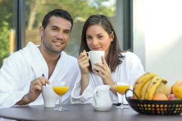 Happy young couple in bathrobes having breakfast outdoors