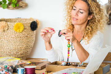 Cheerful woman adult at home doing necklace jewels with colorful beads - home work and alternative...