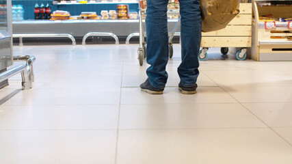Obraz premium Legs of a man standing in the supermarket. Keeping your distance during an epidemic. Protection against a viral epidemic in the city