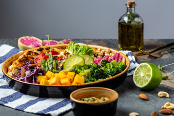 Healthy vegetable buddha bowl lunch with chicken fillet, quinoa, avocado, pumpkin, tomato, broccoli, red cabbage, chickpea, watermelon radish, fresh lettuce salad, nuts on gray background