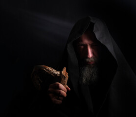 bearded man in a hood with a wooden staff in his hands