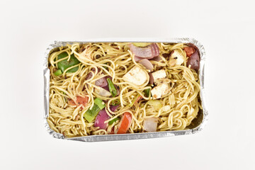 Top view of desi Indian chowmein in foil tray on white background
