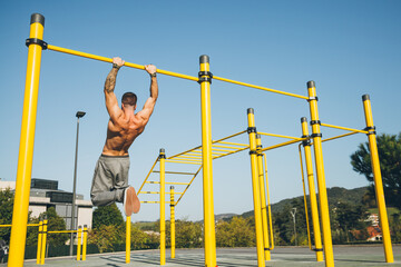 Young athletic man doing gymnastics on bars at a calisthenics park - obrazy, fototapety, plakaty