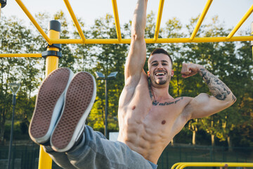 Funny athletic young man hanging from the bars showing his muscles - Powered by Adobe