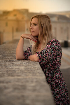 Foto vertical de una mujer rubia pensando apoyada en un muro con el atardecer  en Malta. 