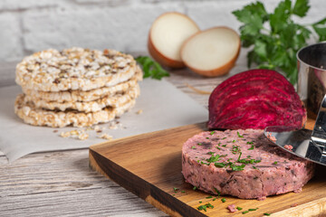 Raw veggie burger with beetroot and white beans with parsley leaves on wood cutting board.