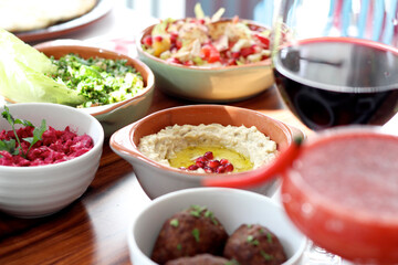 close up of a plate of humus decorated with olive oil and pomegranate seeds on a table surrounded by traditional Lebanese food