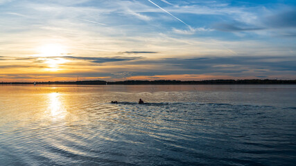 Two people swimming in a lake at sunset