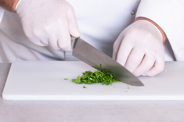 close up of a male chef with gloves using a kitchen knife to chop some parsley on a cutting board