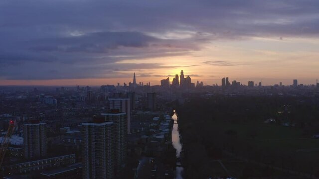 Descending Aerial drone shot of London Canal Victoria park towards city skyline at sunset