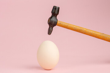 Hammer hit on an egg on pink background
