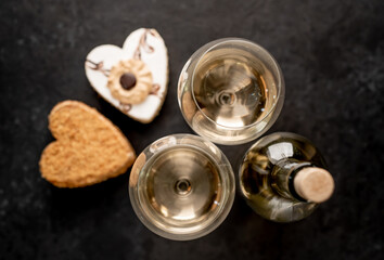 Festive dinner for two for valentine's day. Heart shaped cakes and white wine bottle with glasses on stone background