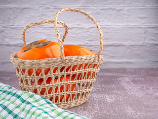 Fototapeta na wymiar Side view of persimmons in a basket with cloth on a wooden table with a white brick wall. Space for text. Concept of health fruit