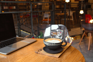 Cozy remote working morning in cafe - cup of delicious cappuccino coffee, protection mask, laptop on desk and books
