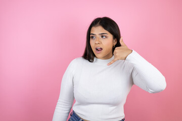 Fototapeta premium Young beautiful woman over isolated pink background confused doing phone gesture with hand and fingers like talking on the telephone
