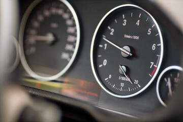 Fototapeta premium Rev counter of car selective focus closeup with copyspace. Tachometer or revolution counter, RPM gauge with red glowing needle on car dashboard with fuel and out of focus speed meter.