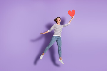 Fototapeta na wymiar Full length photo of charming young woman wear casual outfit looking holding looking red paper heart isolated violet color background