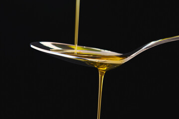 Olive oil liquid on a spoon over black background. Cooking