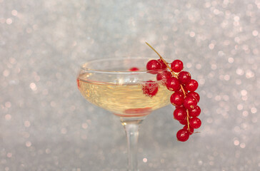 Currant twig on the glass with champagne against silver defocused background. Holidays concept. Greeting, invitation card. Selective focus.