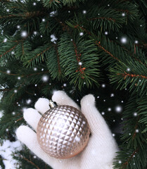 Hand in a white glove with a new year's pink ball on a background of spruce and falling snowflakes in the open air.