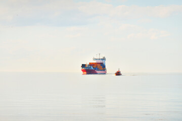 Large cargo container ship being led by the pilot boat. Piloting service. Unknown waters. Global communications, logistics, industry, freight transportation, nautical vessel, nautical route, port © Alex Stemmer