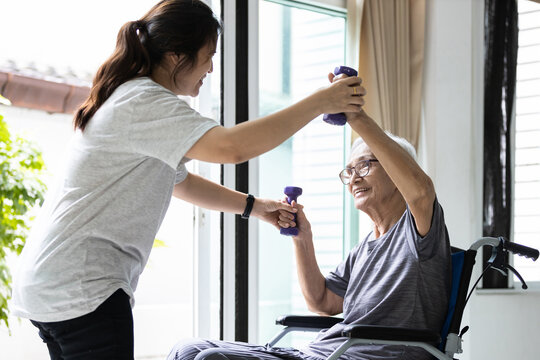 Female physiotherapist working or work out with a senior patient,old elderly exercising with dumbbells,asian caregiver assisting senior woman lifting weights during physical therapy in nursing home.
