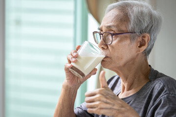 Close up,Asian senior woman drinking fresh milk from the glass,healthy elderly holding glass of milk,old people showing thumb up while drinking,health care,healthy nutrition,food and drinks concept