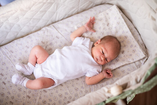 Newborn baby boy in bed. New born child in white bodykit lying in light cradle. Children sleep. Bedding for kids. Infant napping in bed. Healthy little kid shortly after birth