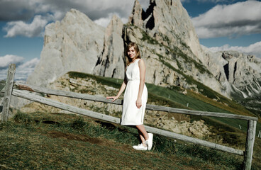 Naklejka premium a young girl in a white dress on the top of the mountain enjoys the sunset against the backdrop of beautiful mountains. travel to the alps. beautiful landscape over the valley. beauty of nature.