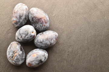 Several ripe organic Damson plums, close-up, on a slate board.