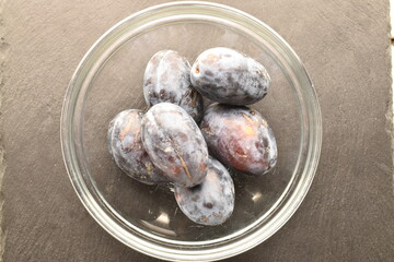 Several ripe organic Damson plums, close-up, on a slate board.