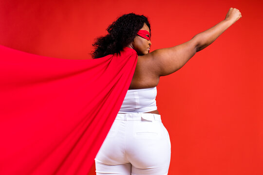 Spanish Woman In Eye Mask And Superhero Cloak In Red Studio Background