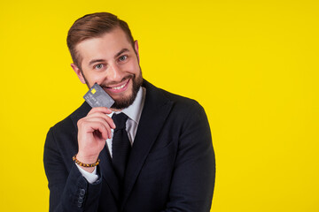 Portrait of handsome young businessman holding credit card over yellow background