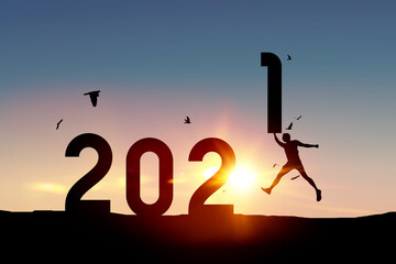 Silhouette man jumping and holding number 1 with birds flying on sunset sky at top of mountain and number like 2021 abstract background.