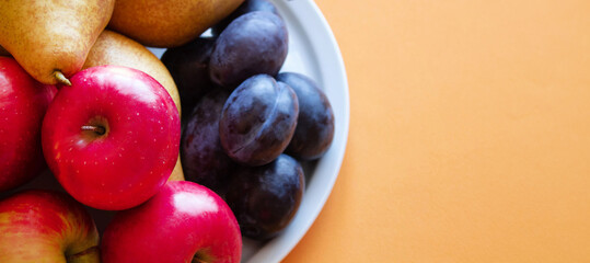 Organic fresh natural red apples, pears and dark blue plums on yellow background