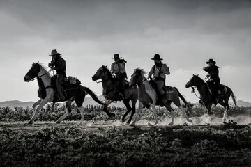 Silhouette, vintage of a group of cowboys riding horses, and shooting a gun