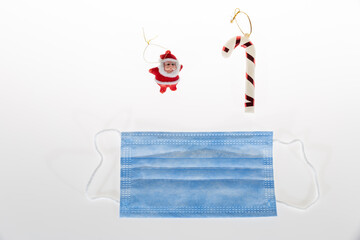 Christmas decoration on white background of candy cane, santa clause miniature and protective medical face mask for Covid-19.