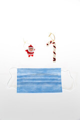Christmas decoration on white background of candy cane, santa clause miniature and protective medical face mask for Covid-19.