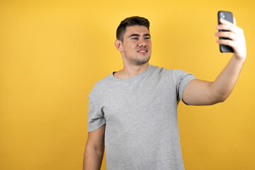 Young handsome man wearing a casual t-shirt over isolated yellow background taking a selfie with his phone