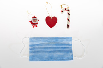 Christmas decoration on white background of candy cane, santa clause miniature, red heart shape and protective medical face mask for Covid-19.